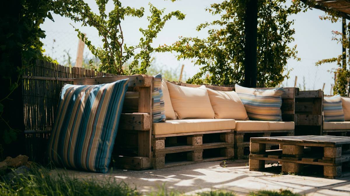 Handcrafted patio dining garden benche can wooden with teak slats and angled supports on stone patio